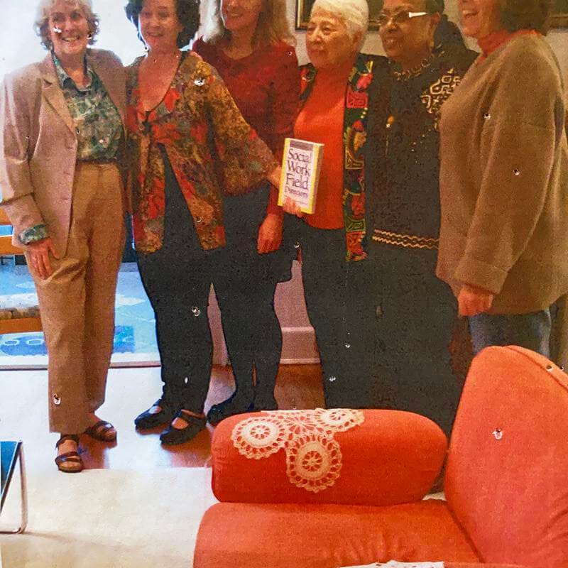 Dr. Gourdine stands in a group of female colleages with a book.